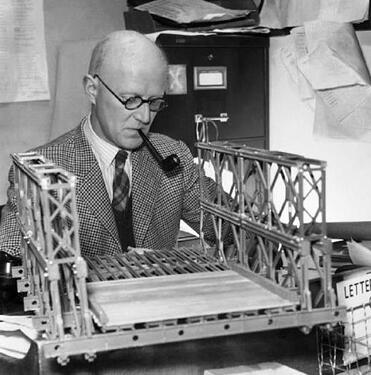 Donald-C-Bailey-examines-the-model-of-a-Bailey-bridge-which-is-resting-on-his-desk.